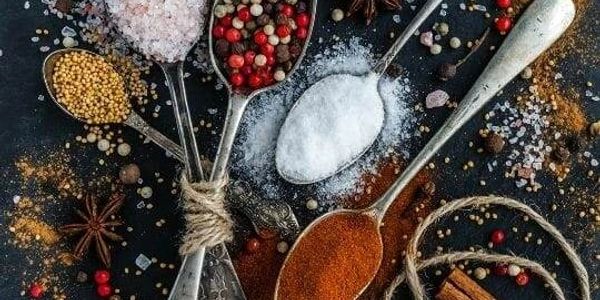 Spoons filled with various colorful spices on a dark surface.