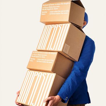 Person in blue jacket carrying stacked cardboard boxes.