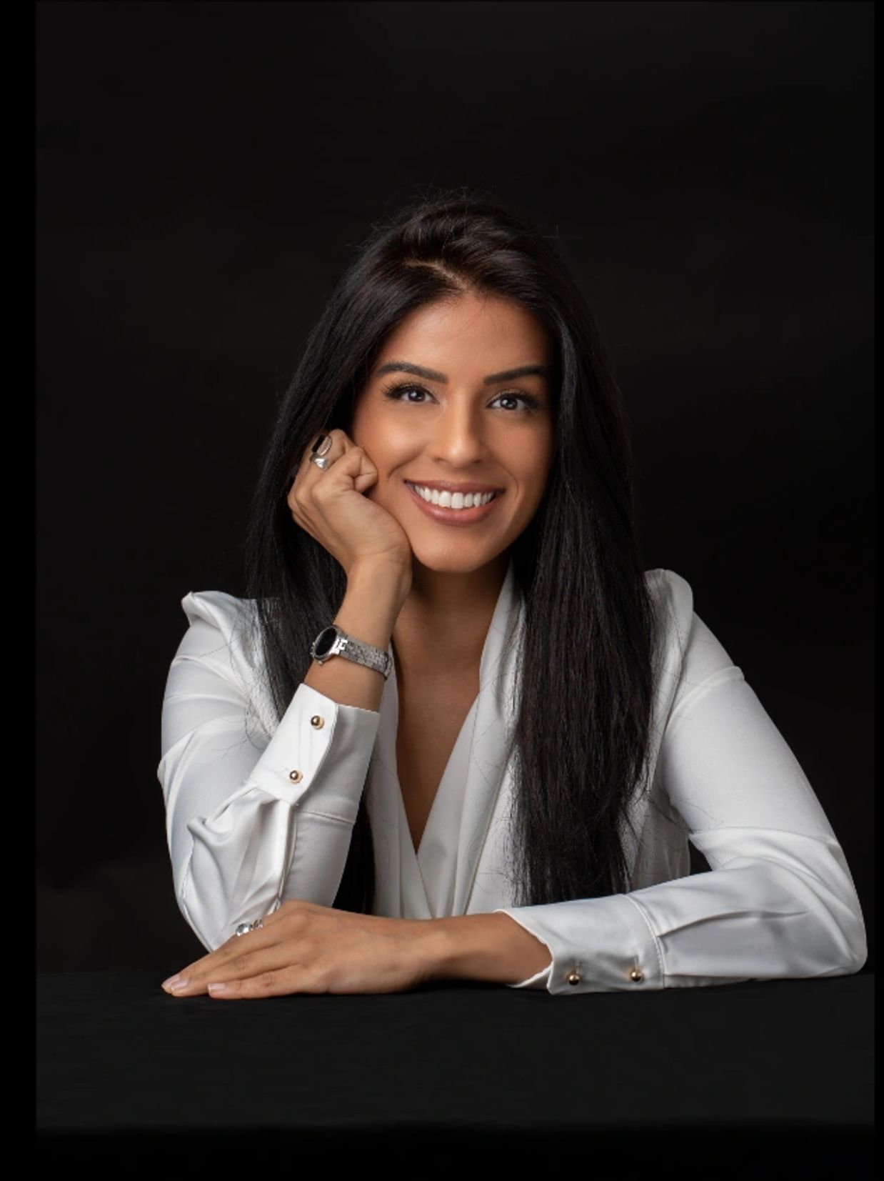 Smiling woman in white blouse against black background.
