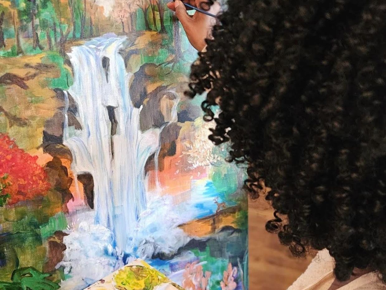 Artist painting a colorful waterfall and forest scene on canvas.