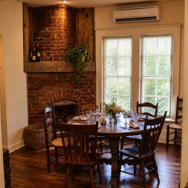Cozy dining room with round wooden table and exposed brick fireplace.