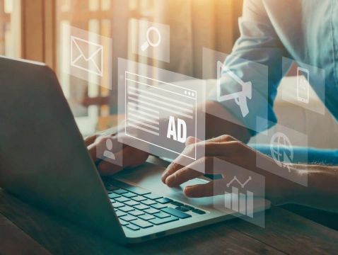 Person sitting at laptop with images of ads, graphs, email and search floating in the air