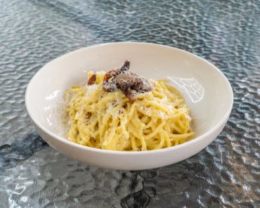 A creamy carbonara pasta dish garnished with grated cheese and mushrooms.