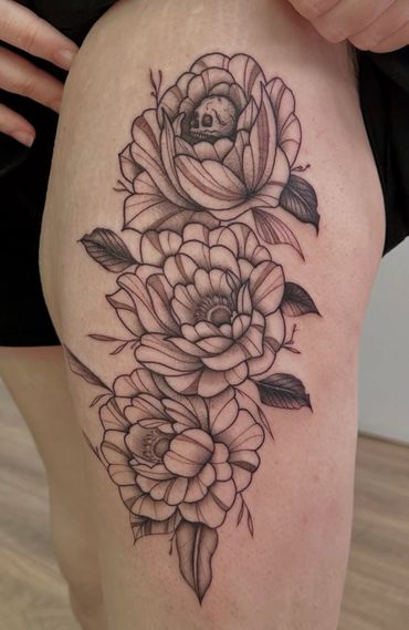 This is a black and grey tattoo of a skull within some florals
