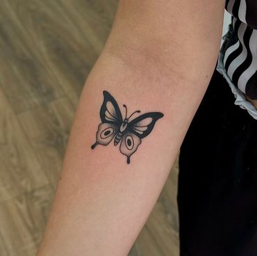 This is a black and grey tattoo of a butterfly in American traditional tattoo style