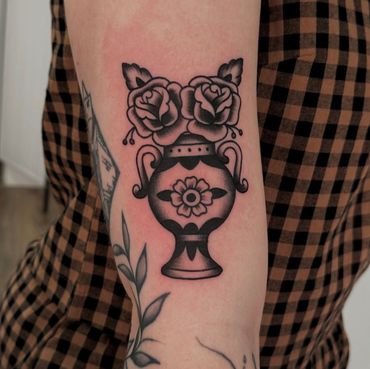 This is a black and grey tattoo of a vase with roses in American traditional tattoo style