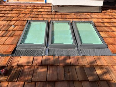 Three skylights on a wooden shingle roof under sunlight.