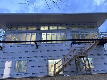 Two-story house under construction with multiple windows and temporary wooden stairs.