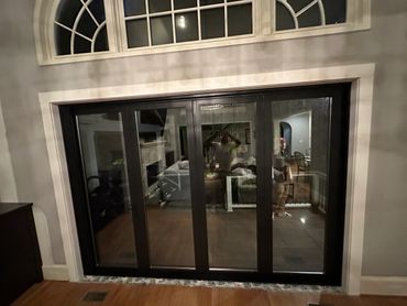 Dark-framed sliding glass doors reflecting an indoor living space and two people.