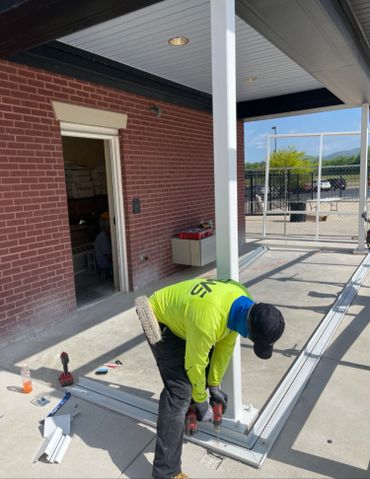 Worker in bright yellow shirt drilling near a white post on a concrete floor.