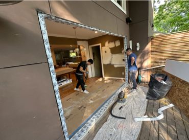 Two men working on a large window installation in a home.