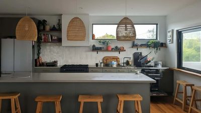 Modern kitchen with wooden stools and wicker pendant lights.