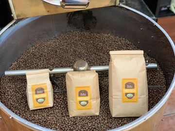 Three bags of D&A Coffee Beans placed on freshly roasted coffee beans in a roaster.