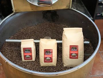 Three bags of coffee displayed on roasted coffee beans inside a large roasting drum.