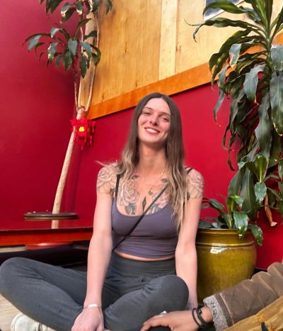 A smiling young woman sitting cross-legged indoors.