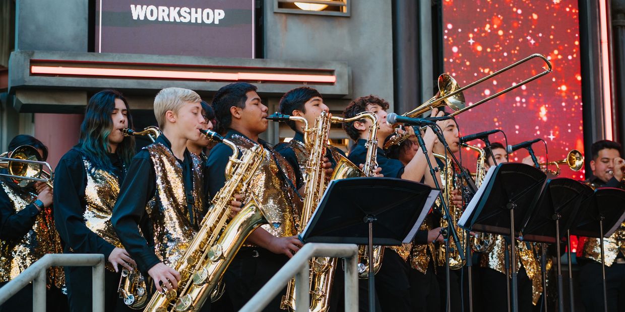 A group of young musicians in gold vests playing saxophones and trombones on stage.