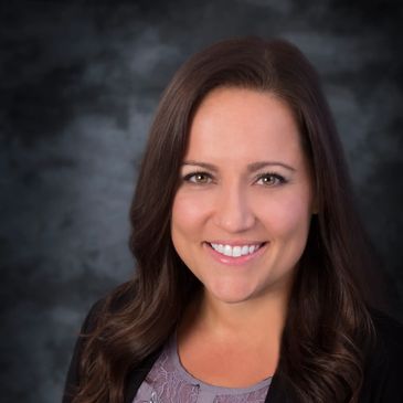 Smiling woman with long brown hair wearing a butterfly-patterned blouse and black blazer.