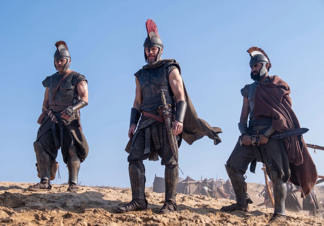 Three warriors in ancient armor standing on a sandy hill.