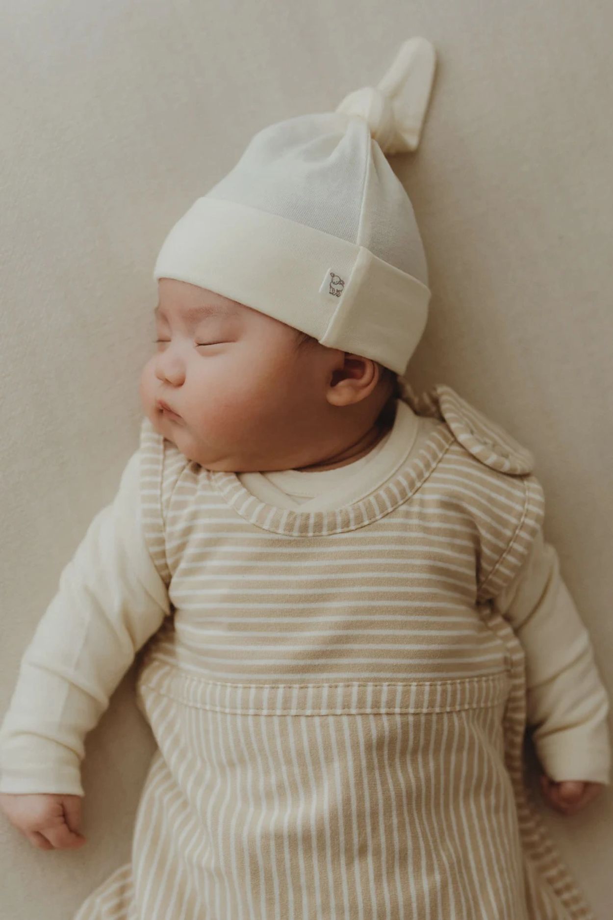 Sleeping baby wearing a white hat and beige striped outfit.
