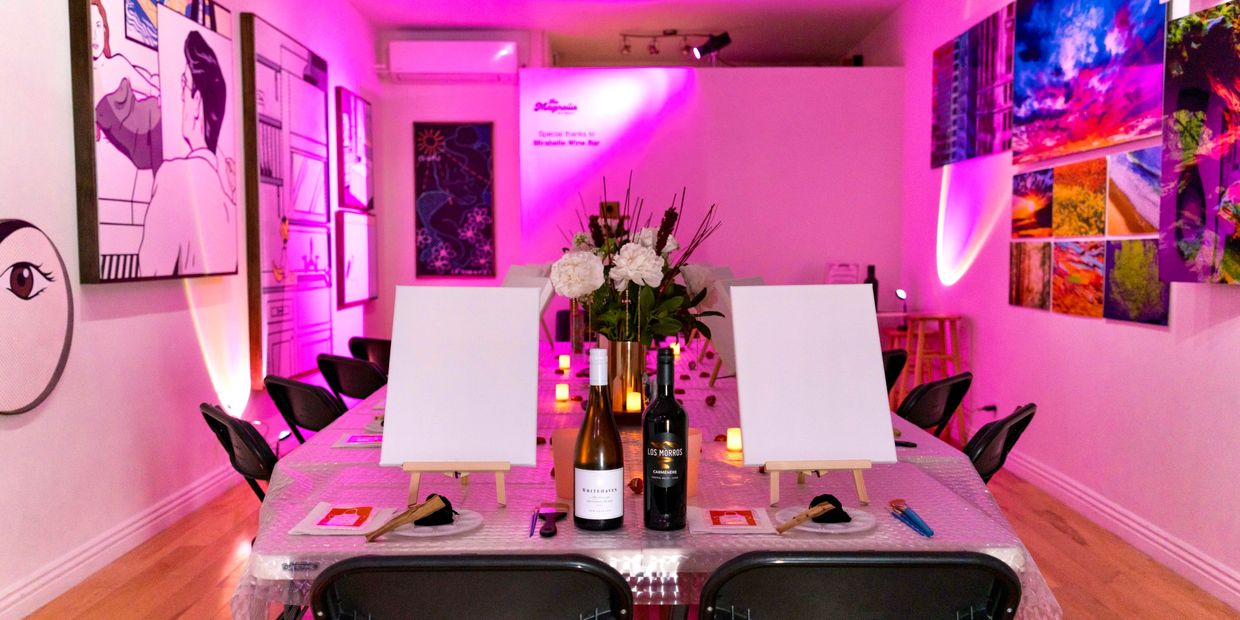 Art studio setup with canvases, wine bottles, and pink lighting.