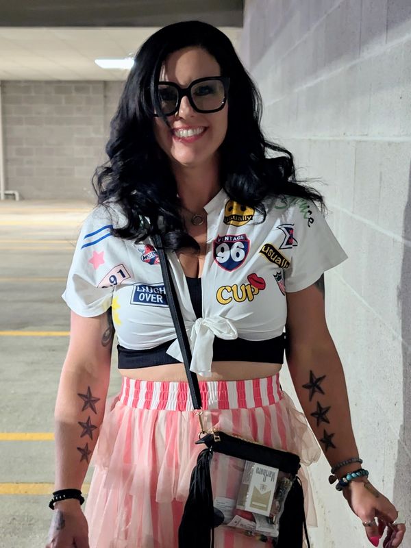 Smiling woman with glasses and star tattoos, wearing a colorful outfit.