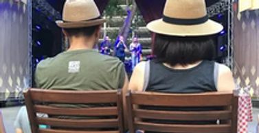 Two seated people on wooden seats wearing straw hats as seen from behind
