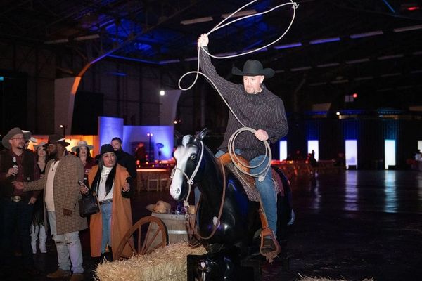 A man is sitting on a statue of a horse, twirling a rope in his hands