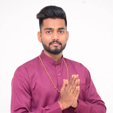 Man greeting with folded hands wearing maroon traditional attire.