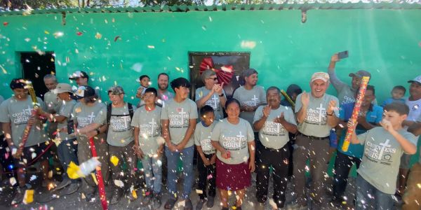 Group celebration with confetti and matching shirts outside a turquoise building.