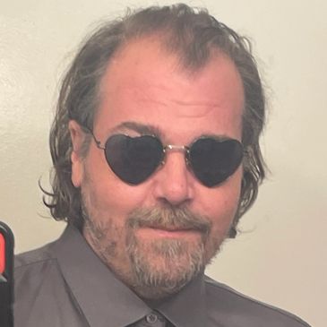 Man with heart-shaped sunglasses and a slight smile.