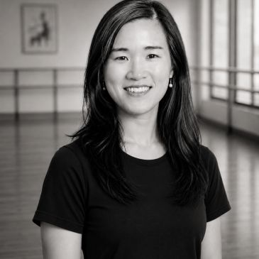 A smiling woman in a black shirt in a spacious room.