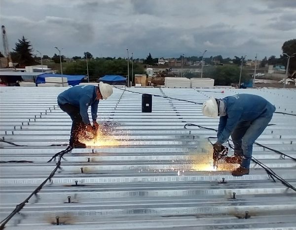 Two workers welding metal on a rooftop with sparks flying.