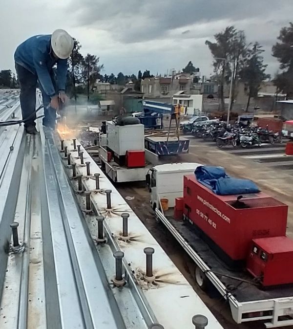 Worker welding metal roofing on a construction site under cloudy skies.