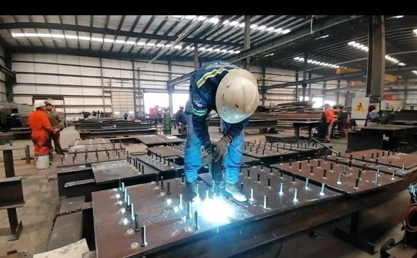 Worker welding metal in a large industrial workshop.