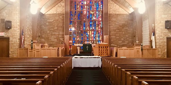 Interior of a church with wooden pews and colorful stained glass window.