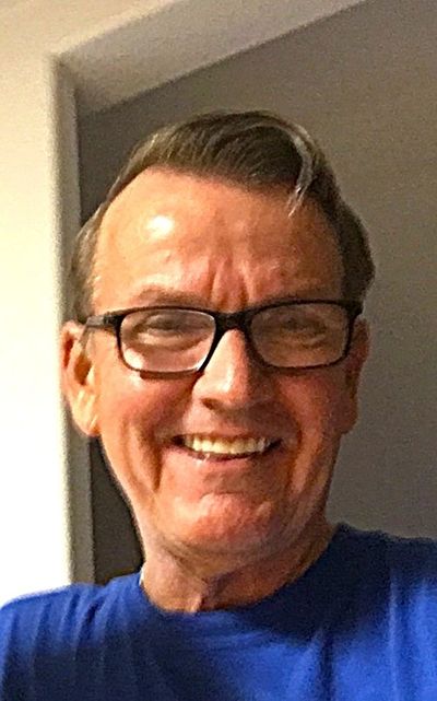 Smiling man wearing glasses and a blue shirt indoors.
