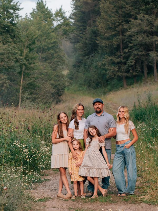 Family of six posing outdoors on a trail surrounded by trees.