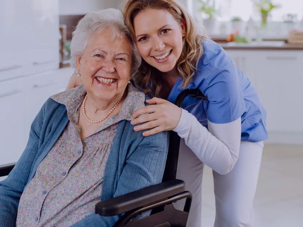 Smiling elderly woman in wheelchair with caring nurse.