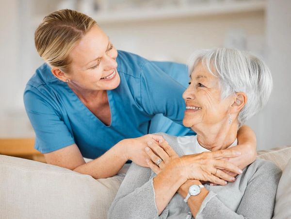 Caregiver warmly embraces elderly woman, sharing a joyful moment.