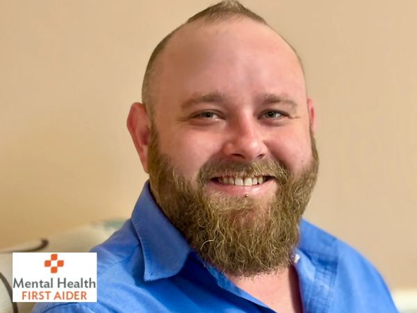 Smiling bearded man in blue shirt sitting indoors.