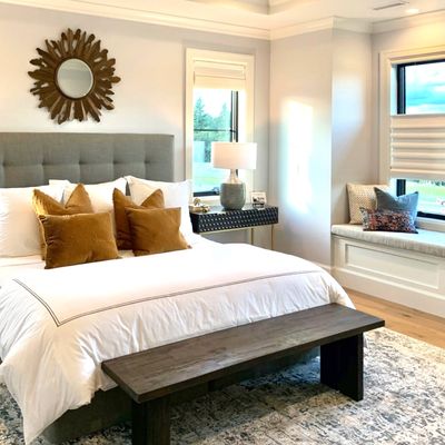 Nicely made bed with a duvet, pillows, mirror above, and a bench at the foot of the bed.