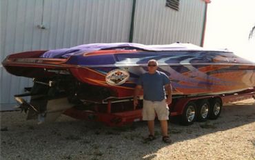 Man standing beside a large, colorful speedboat on a trailer.