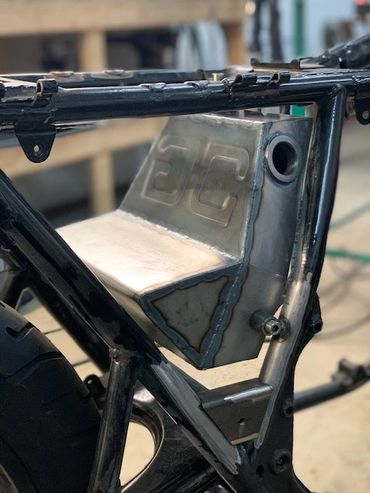 A custom metal motorcycle fuel tank mounted on a black motorcycle frame.