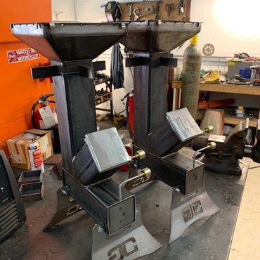Two metal industrial machines with funnels on a workbench in a workshop.