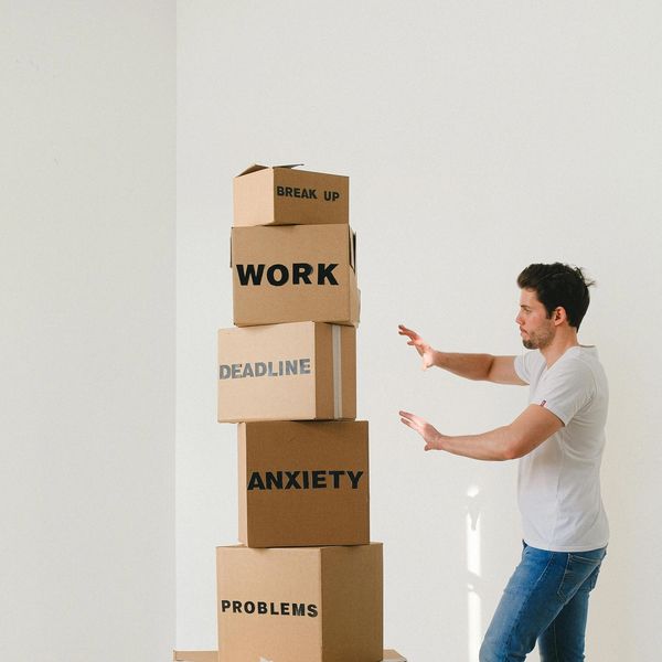 Man balancing boxes labeled with stress factors like work and anxiety.