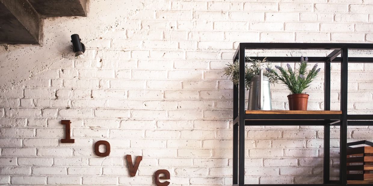 Modern shelf with plants and love letters on white brick wall.