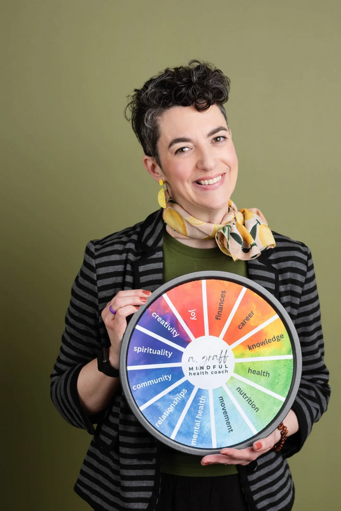 Smiling health coach holding a colorful wellness wheel with various life aspects.