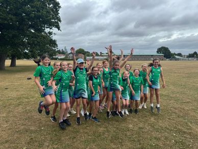 Girls in green sports uniforms jumping joyfully on a field.