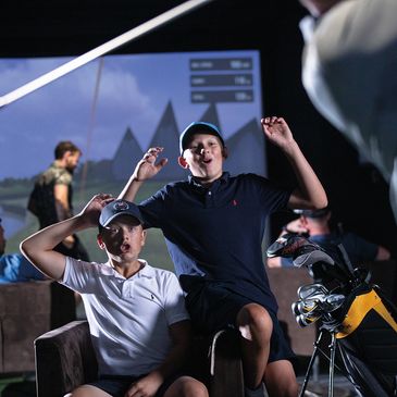 Two boys celebrating indoors with golf equipment and a golf simulator.