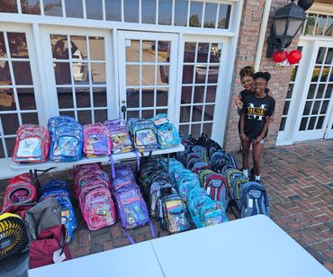 Two people posing with colorful backpacks on display outside a building.